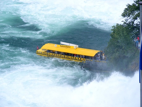 Ein gelbes Felsenfahrt-Boot legt am begehbaren Felsen in der Mitte des Rheinfalls an.