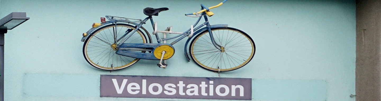Ein an einer Hauswand aufgehängtes Fahrrad weist auf einen Abstellplatz für Fahrräder hin.