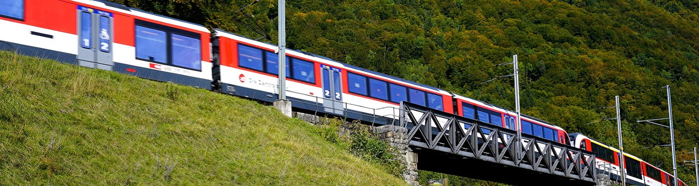 Ein Regionalzug der Schweizer Zentralbahn fährt über eine von Wäldern eingerahmte Eisenbahnbrücke.