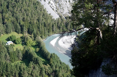 Der türkisblaue Rhein schlängelt sich zwischen einer bewaldeten Steilwand und einer kiesigen Landzunge hindurch.